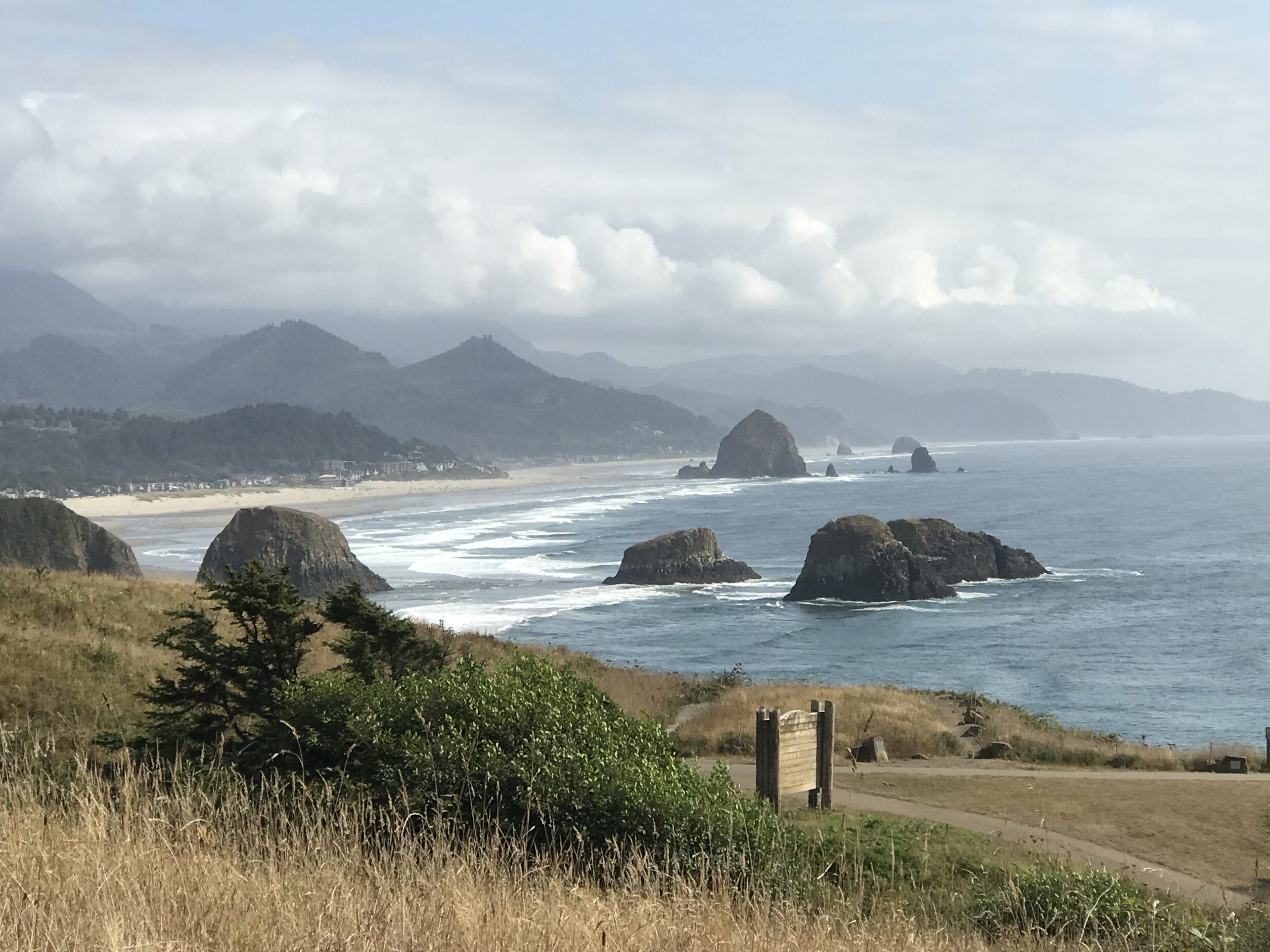 Haystack Rock at Cannon Beach, Oregon, with rugged coastline and misty mountains in the background.