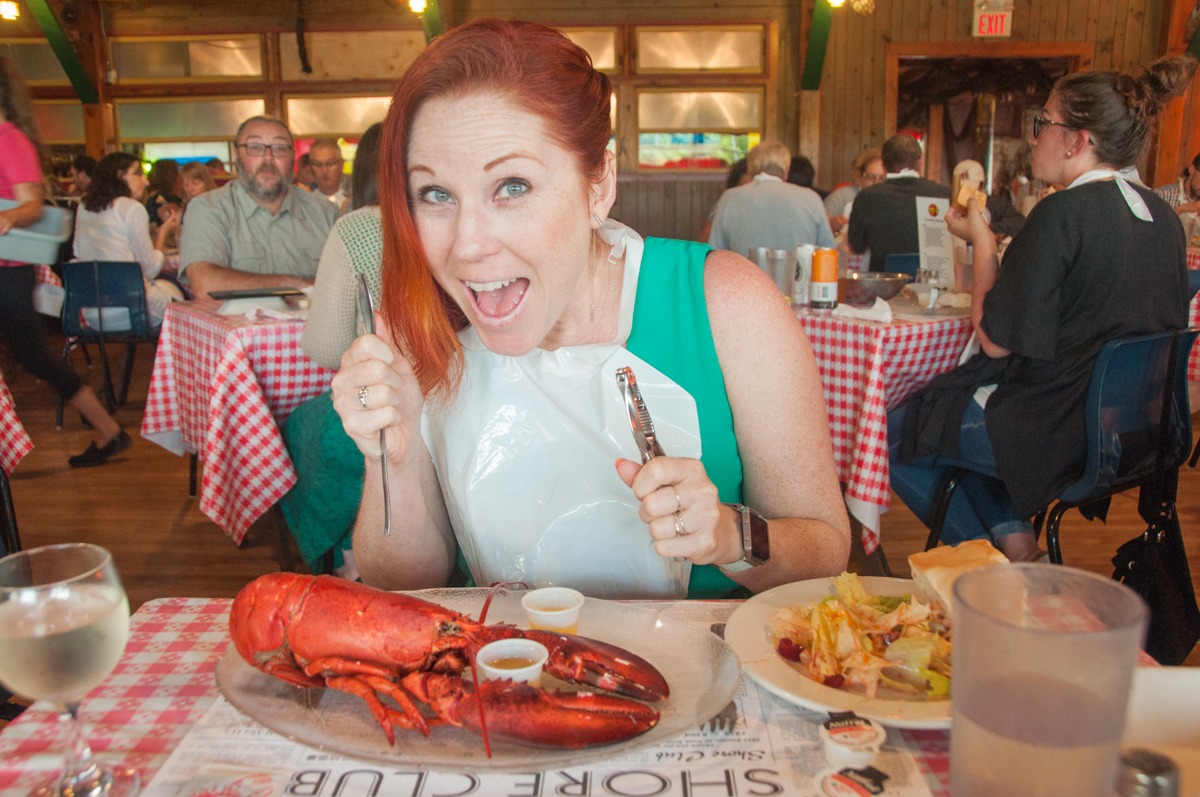 Excited woman with lobster, bib, and tools at a restaurant. Ready to eat!