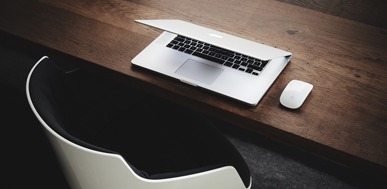 Laptop and mouse on wooden desk with modern chair. Minimalist workspace.