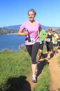 Woman running a race with number 343 on a scenic trail overlooking the water.