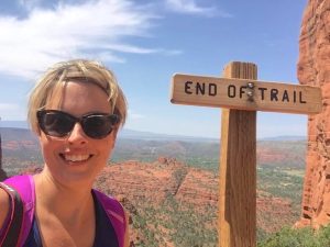 Woman at the "End of Trail" sign in Sedona, Arizona, with red rock formations in the background.