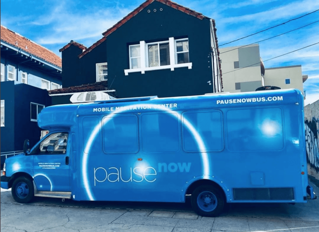 Blue "Pause Now" mobile meditation center bus parked on a city street. PauseNowBus.com is visible.