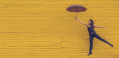 Woman floating with an umbrella against a yellow wall.