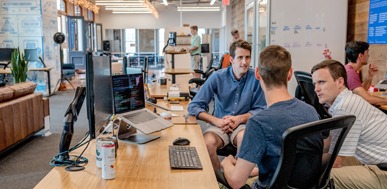 Office team collaborating, discussing project at desk with laptops and computers.