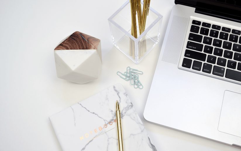 Freelancing concept: Laptop, notebook, pen, and desk accessories on a white workspace.