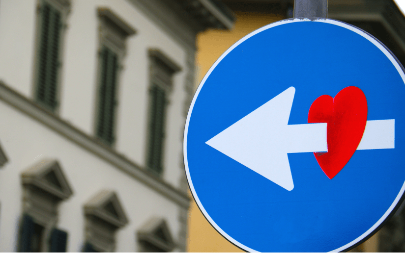 Street sign with a left arrow piercing a red heart, symbolizing tough love.