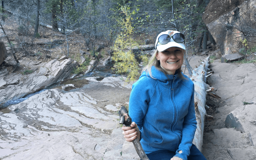 Gretchen Harding hiking in nature, smiling with a walking stick.