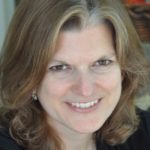 Woman with graying hair smiles, likely during a presentation or public speaking event.