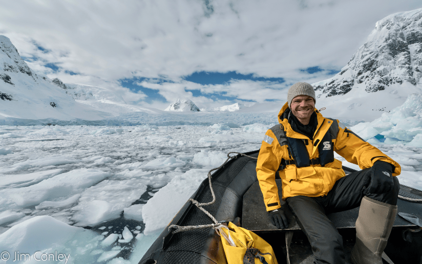 Jim Conley on a boat amidst ice floes in Antarctica, wearing a yellow jacket.