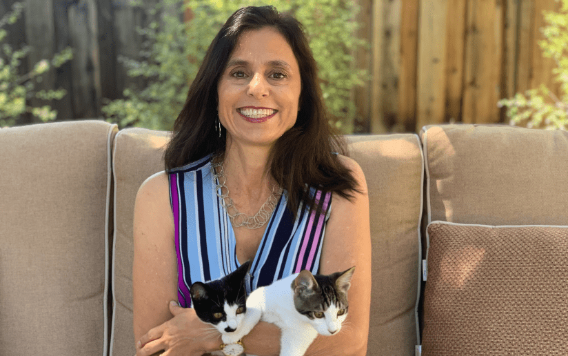 Kristine Duffy smiling with two cats on an outdoor couch.