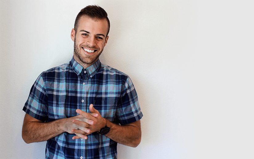 Kyle Courtright smiling in a blue plaid shirt against a white wall.