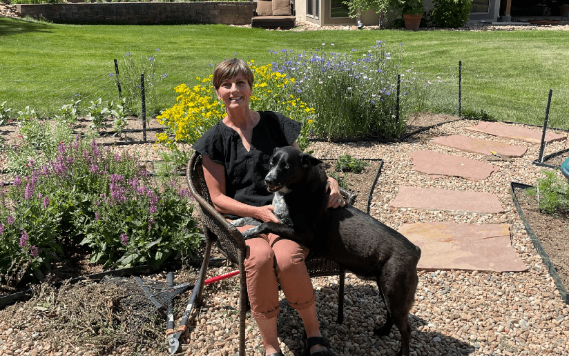Liz Tobiason sits with her dog in a sunny garden setting.