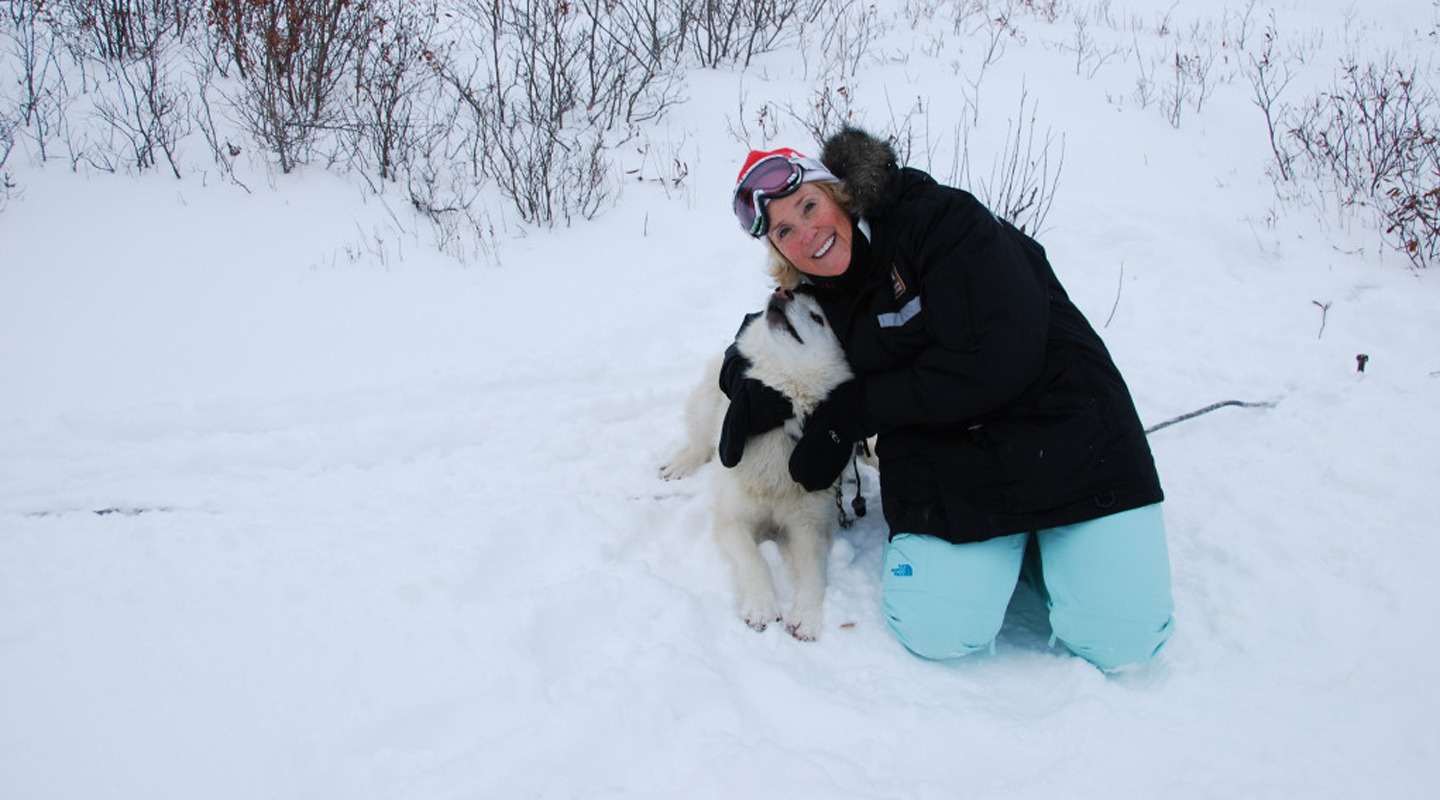 Nancy Keith Kelly embraces a dog in the snow, enjoying an outdoor adventure.