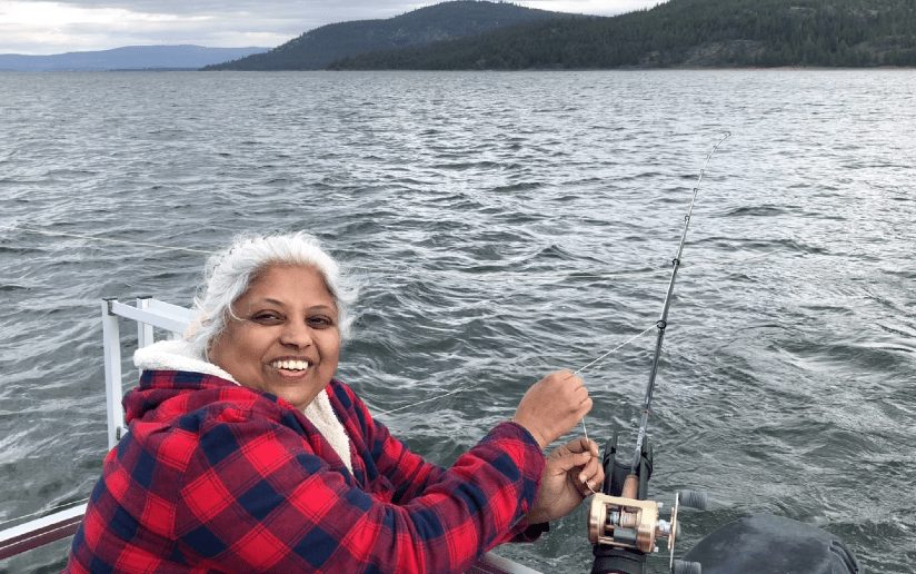 Sandeepa Nayak fishing on a lake, smiling and holding a fishing rod.