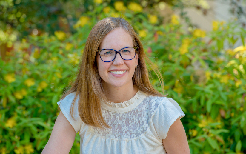 Yvonne Schmidt smiles, posing in front of a yellow flowering bush.