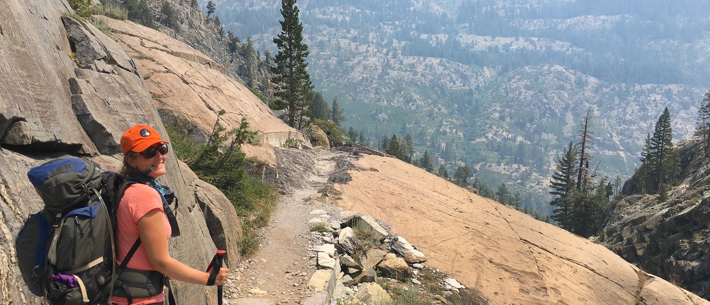 Alexis Keenan hiking a mountain trail, wearing an orange hat and backpack. Next-Gen Consultants.