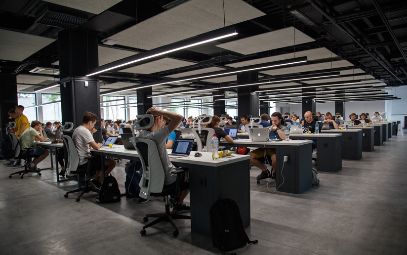 Busy open-plan office with rows of employees working at desks with laptops.