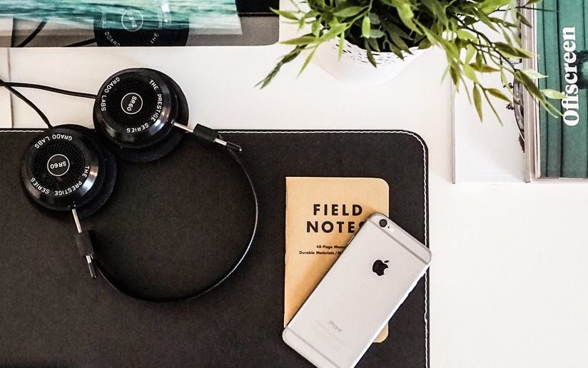 Grado SR60 headphones, Field Notes notebook, and iPhone on a desk. Offscreen magazine visible.