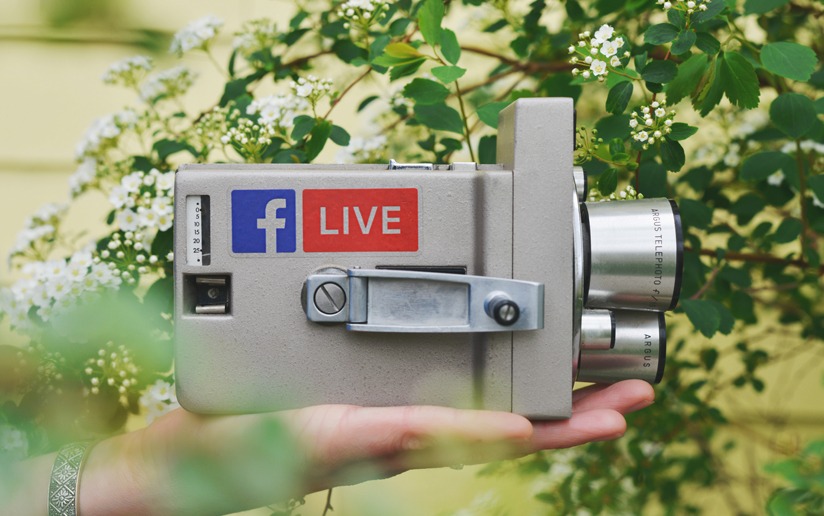 Vintage Argus camera with a Facebook Live sticker, held in hand against a floral background.