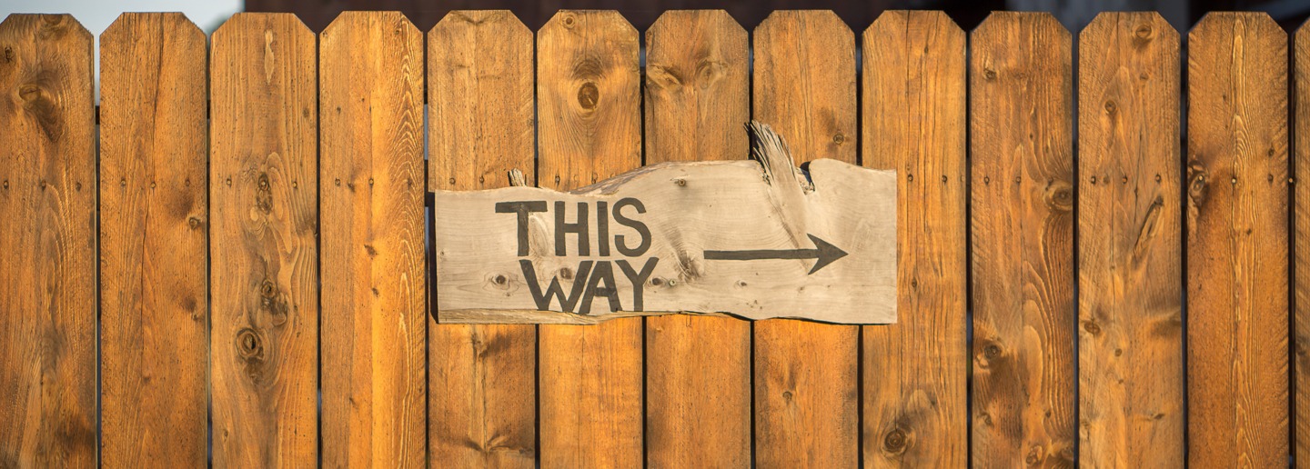 Wooden sign on fence reading THIS WAY with arrow, pointing to the right.
