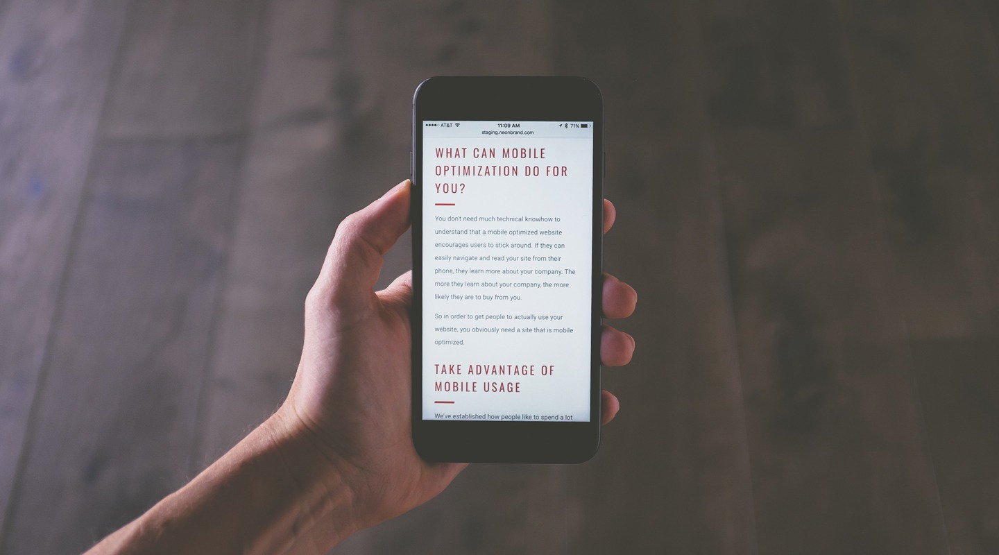 Hand holding smartphone displaying mobile optimized website text: What Can Mobile Optimization Do For You?
