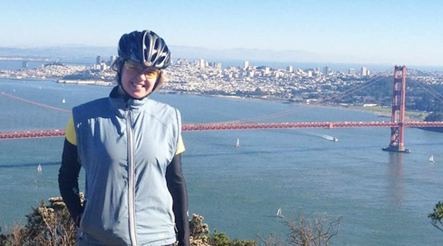 Ruta Jaks smiles in cycling gear with the Golden Gate Bridge and San Francisco skyline behind her.