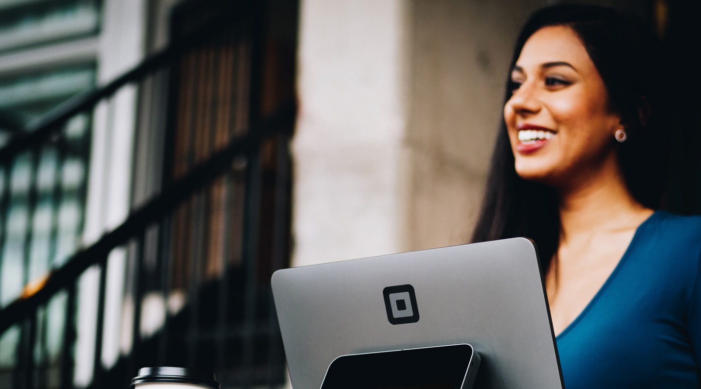 Woman smiling near a laptop with the Square logo and a coffee cup