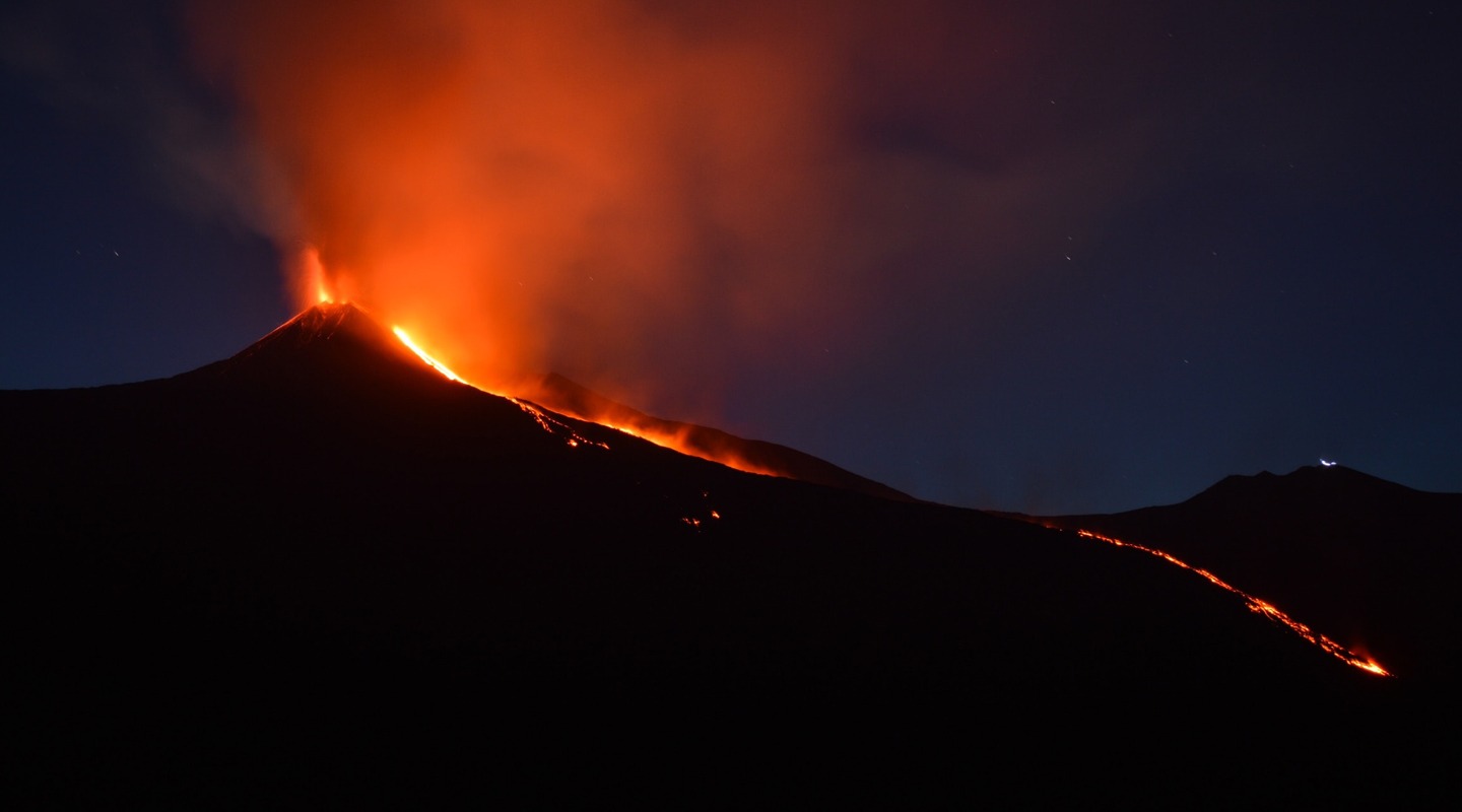 Volcano erupting at night, with fiery lava flowing down the mountain.