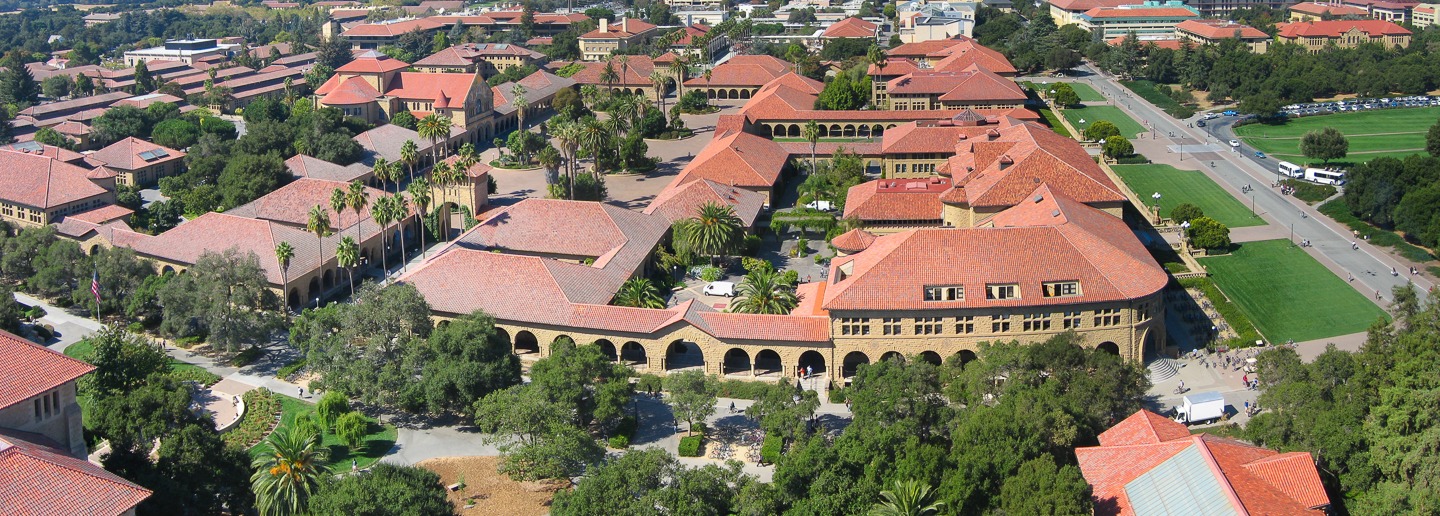 Aerial view of Stanford University campus with red-tiled roofs and green spaces.