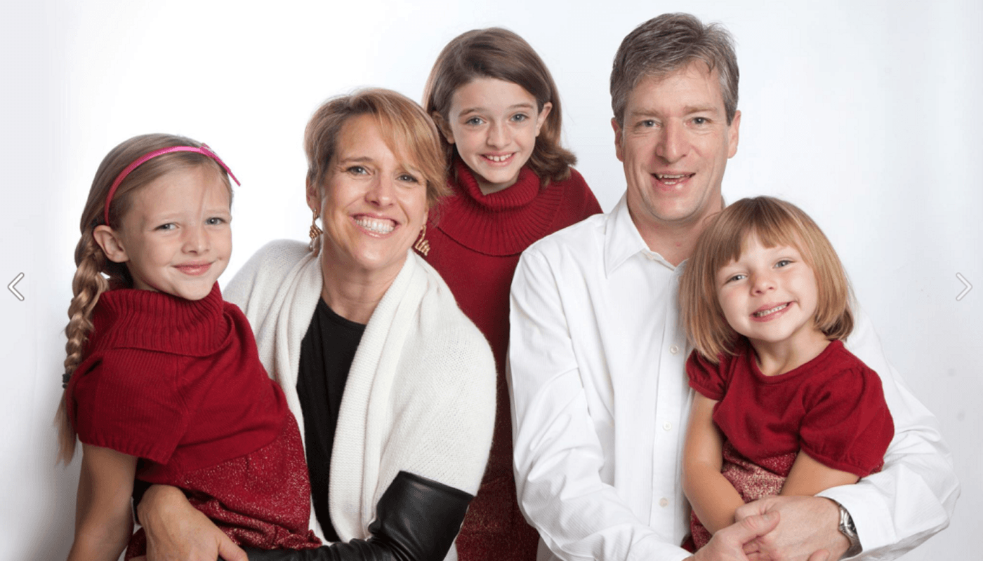 Family portrait: mother, father, and three daughters smiling in red and white.