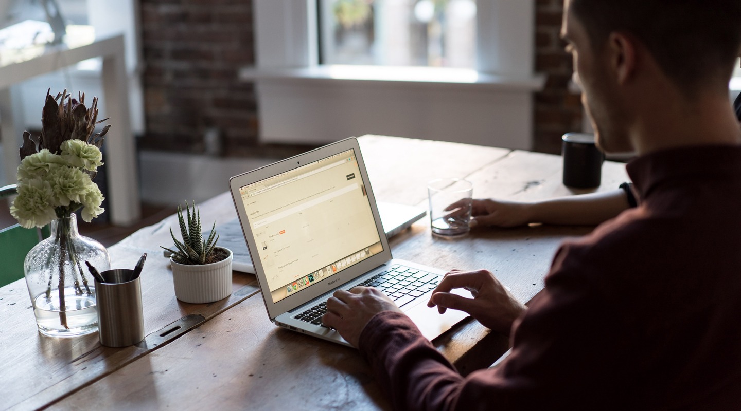 Man using laptop for customer research, likely UserTesting.com, at a wooden table