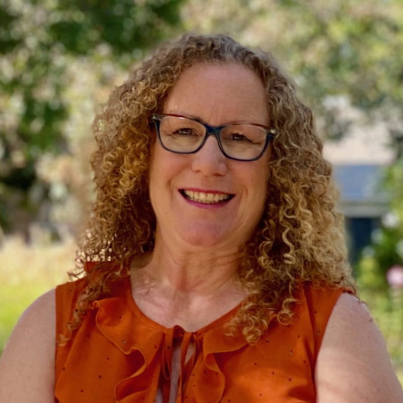 Woman with curly hair and glasses smiling outdoors